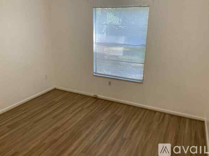 A room with wooden flooring and a window with blinds.