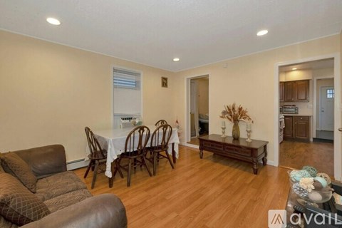 A living room with a brown leather couch, a white dining table with chairs, and a wooden coffee table.