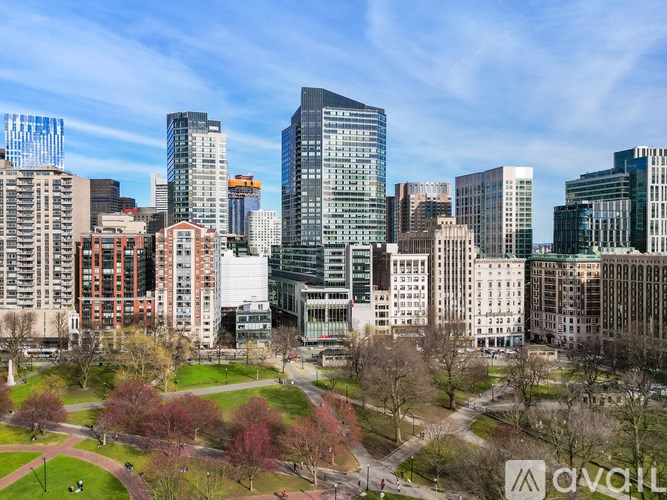 A cityscape with a mix of modern and older buildings, a park with trees, and a clear sky.
