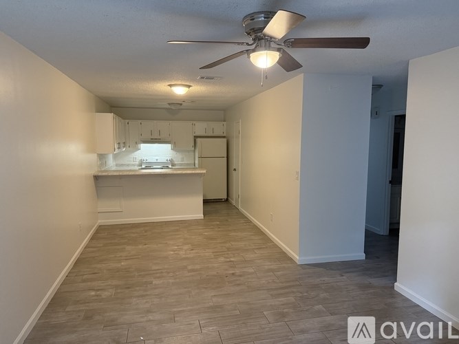 A room with a ceiling fan and a kitchenette in the background.