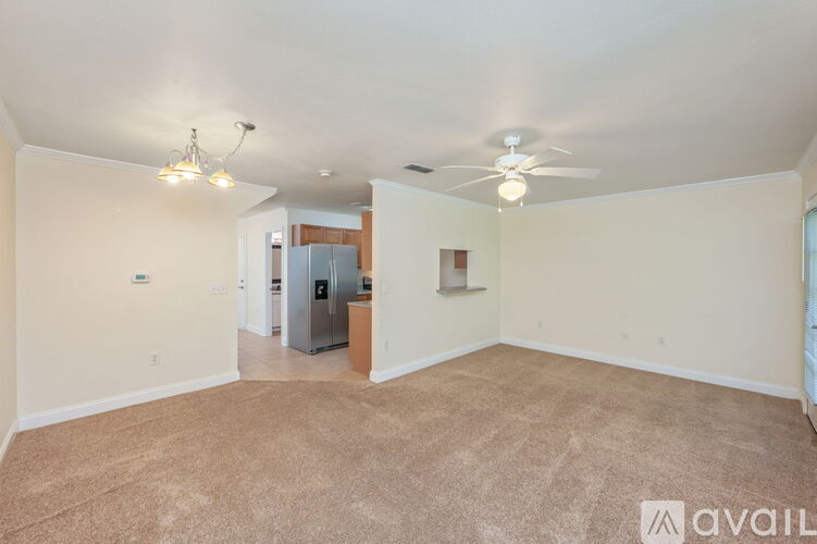A spacious room with a carpeted floor, a ceiling fan, and a kitchenette in the background.