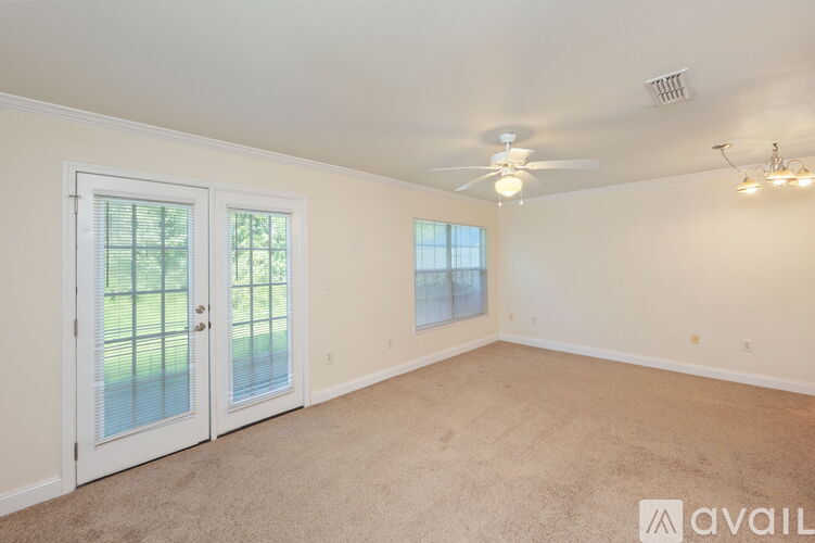 A room with a carpeted floor, a ceiling fan, and a door with a view of a fence and trees outside.