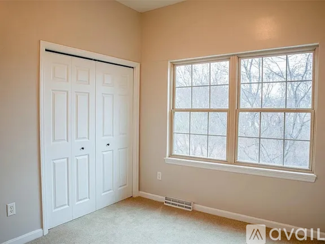 A room with a white door and a window with a view of trees outside.