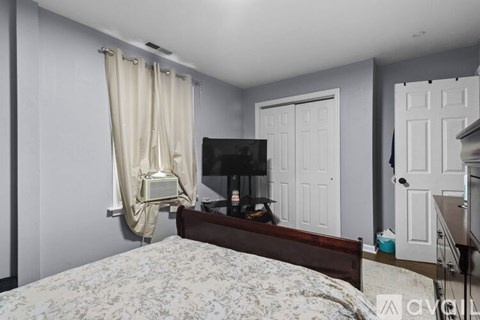 A bedroom with a bed, a television, and a window with curtains.