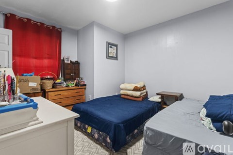 A bedroom with two beds, one covered in a blue sheet and the other in a grey sheet, a dresser, and a small table.