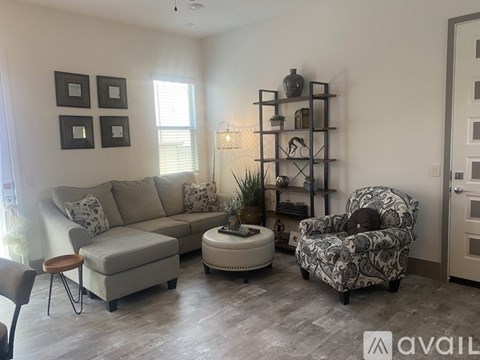A living room with a grey couch, a patterned armchair, and a small table with a plant on it.