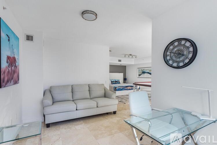 A living room with a grey sofa, glass table and a painting of a bird on the wall.