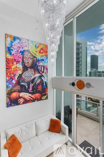 A modern living room with a large painting on the wall and a chandelier hanging from the ceiling.