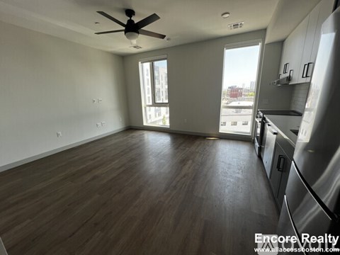 A spacious kitchen and living room with wood flooring and a ceiling fan.