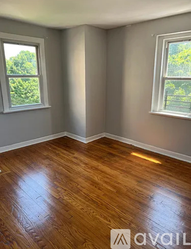 A room with wooden flooring and two windows.