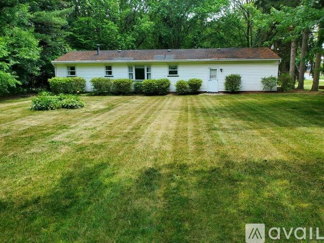 A white house with a red roof is surrounded by green grass and trees.