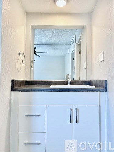 A bathroom with a mirror, sink, and cabinets.