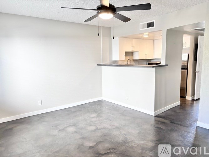A room with a ceiling fan and a kitchen in the background.