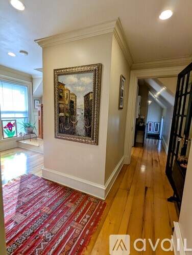 A large painting hangs on a wall above a red carpet in a spacious room.
