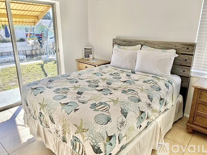 A bed with a leaf patterned comforter is in a room with a sliding glass door.