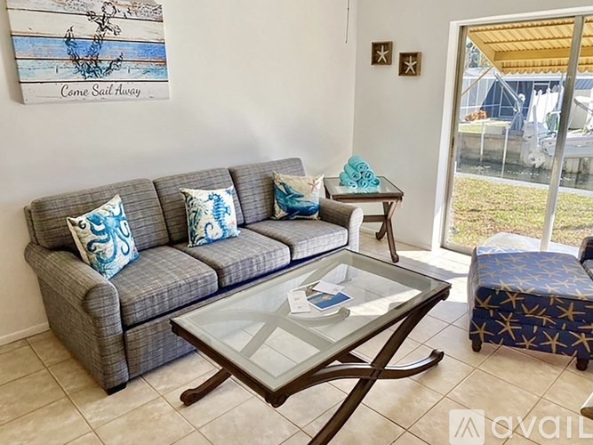 A living room with a grey couch, a glass coffee table, and a painting on the wall.