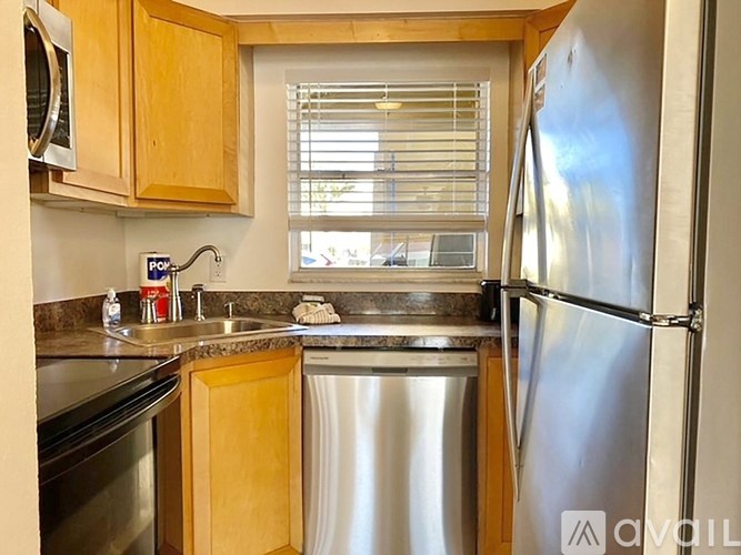 A kitchen with a stainless steel refrigerator, sink, and wooden cabinets.