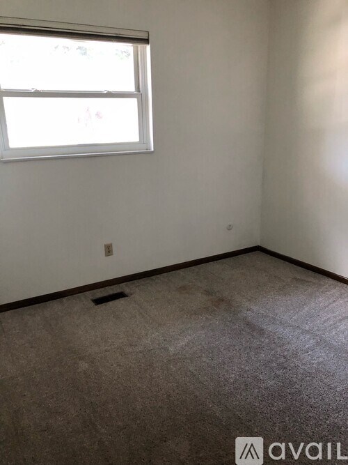 A room with a window and a carpeted floor.