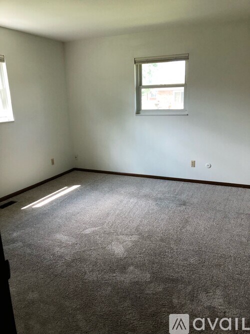 A carpeted room with a window and a wall socket.