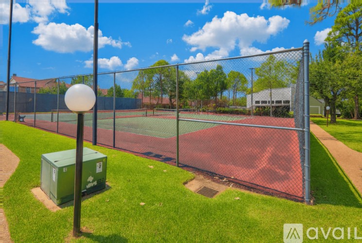 A tennis court is surrounded by a fence and there is a green container on the ground.