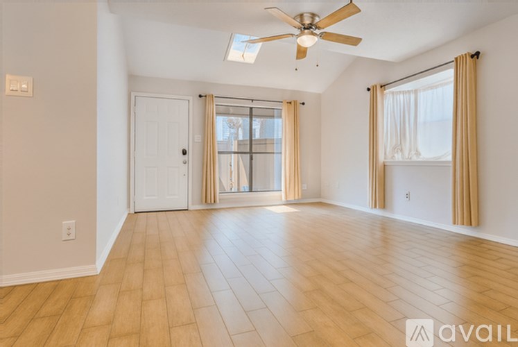 A spacious room with a ceiling fan and light, hardwood floors, and a sliding glass door leading to a balcony.