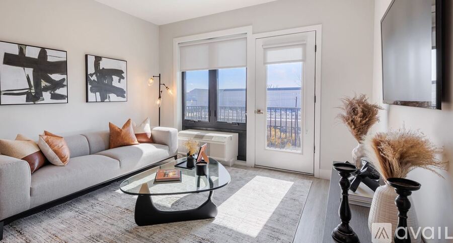 A living room with a grey couch, a glass coffee table, and a large window.