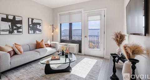 A living room with a grey couch, a glass coffee table, and a large window.