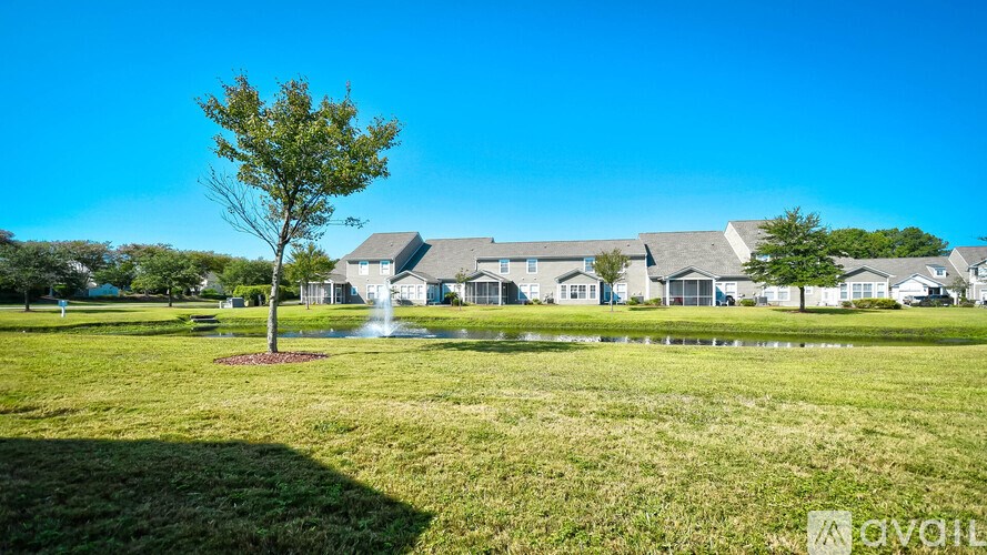 A tree stands in a grassy field with houses in the background.