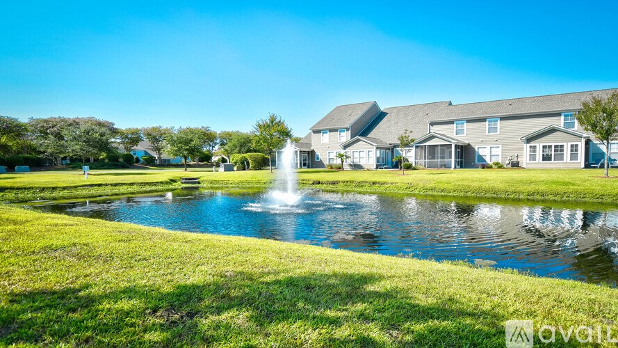 A fountain in the middle of a grassy area with houses in the background.