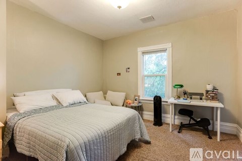 A bedroom with a bed, desk, chair, and window.