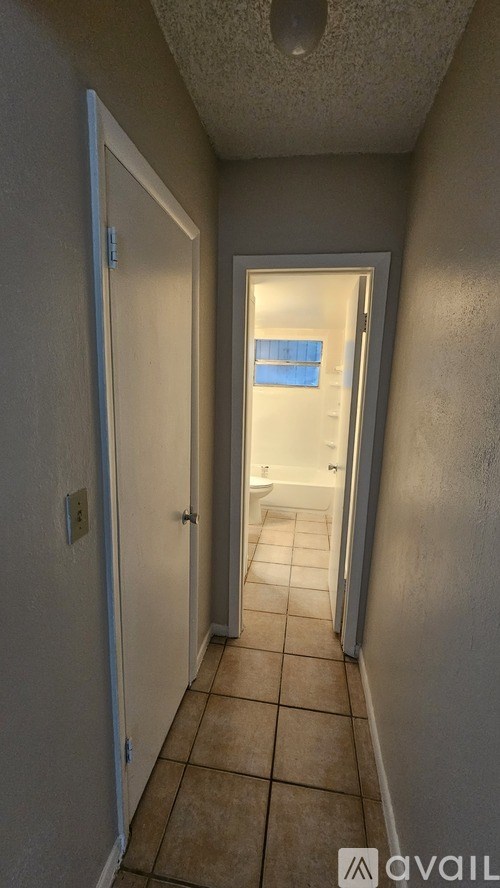 A hallway with a door on the left and a bathroom on the right.