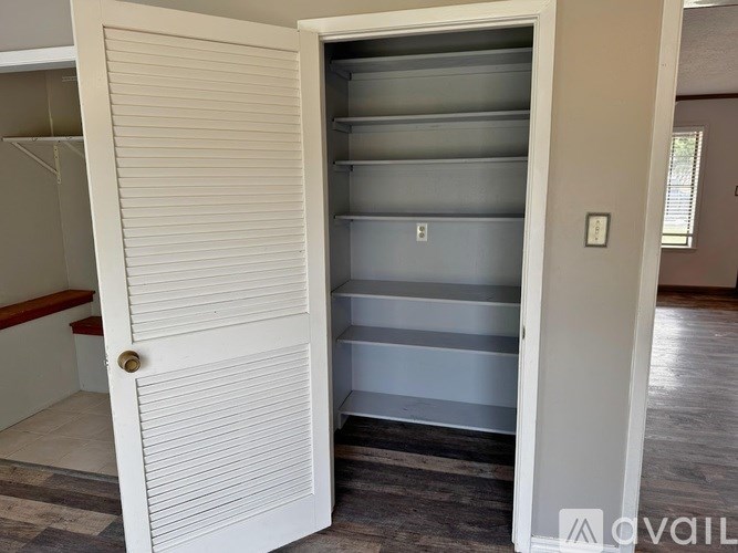 A white door with a gold handle is open to a room with a grey fridge.