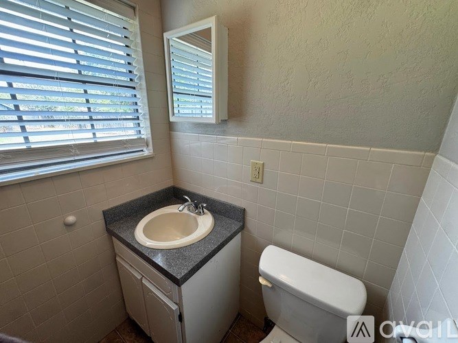 A bathroom with a sink, toilet, and a window with blinds.