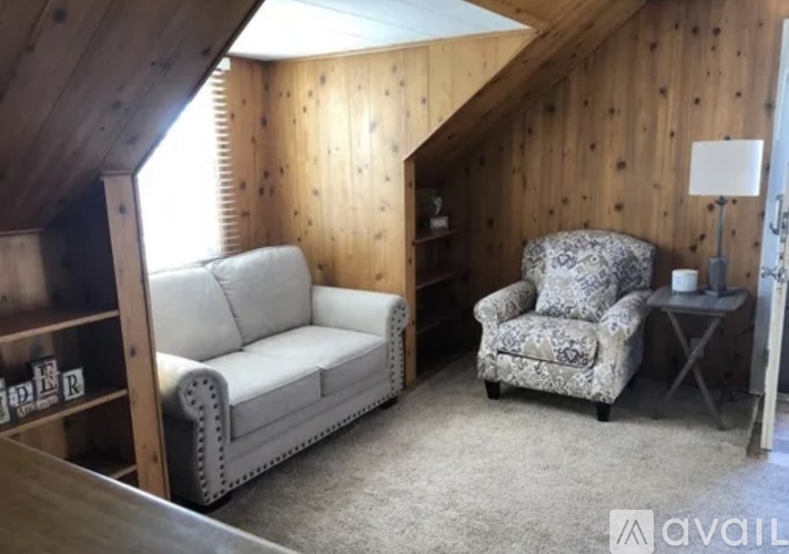 A living room with a couch, chair, and wooden walls.
