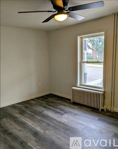 A room with a ceiling fan and a window with a view of the street outside.