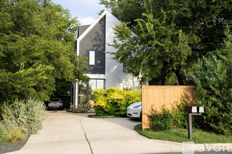 A modern house with a black and white exterior is surrounded by greenery.
