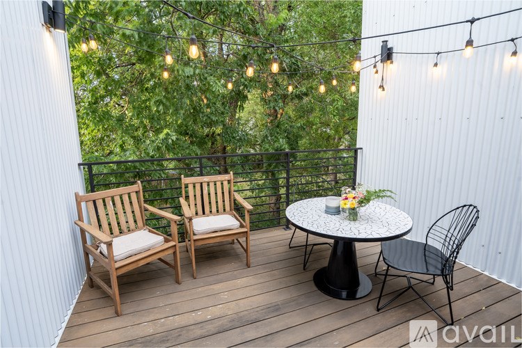A small balcony with a table, two chairs and string lights.