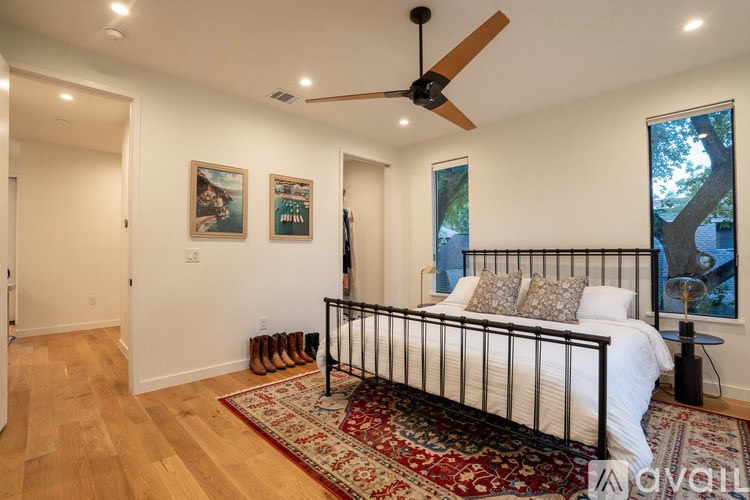 A bedroom with a bed, a rug, a ceiling fan, and pictures on the wall.