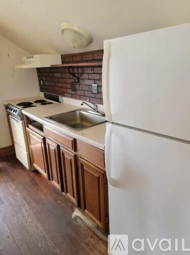 A kitchen with a white fridge, wooden cabinets and a brick backsplash.