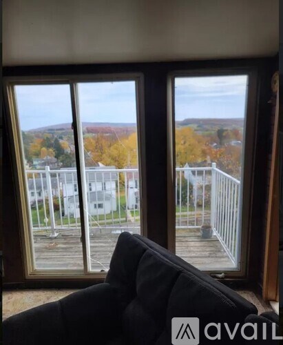 A black couch is in front of a window with a view of a residential area.