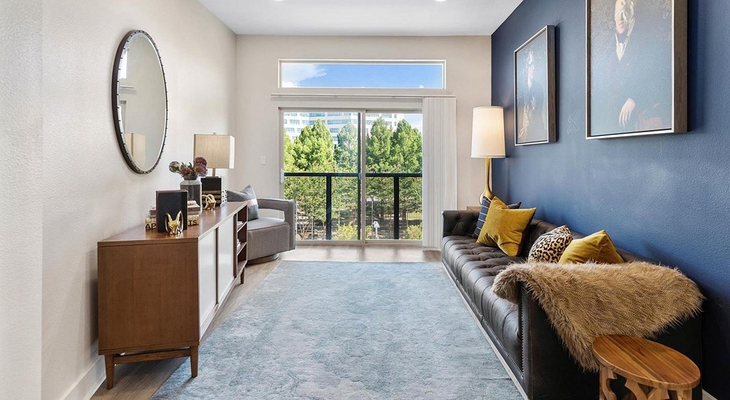 A living room with a black couch and a round mirror on the wall.