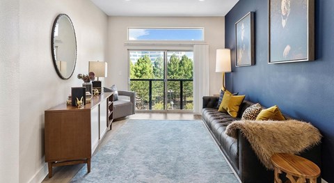 A living room with a black couch and a round mirror on the wall.