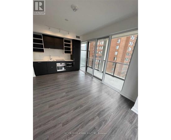 A spacious room with wood flooring and a kitchen area with a stove and cabinets.