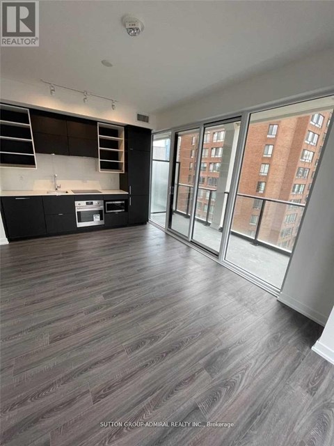 A spacious room with wood flooring and a kitchen area with a stove and cabinets.