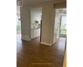 A room with wooden floors and white walls, with a doorway leading to another room.