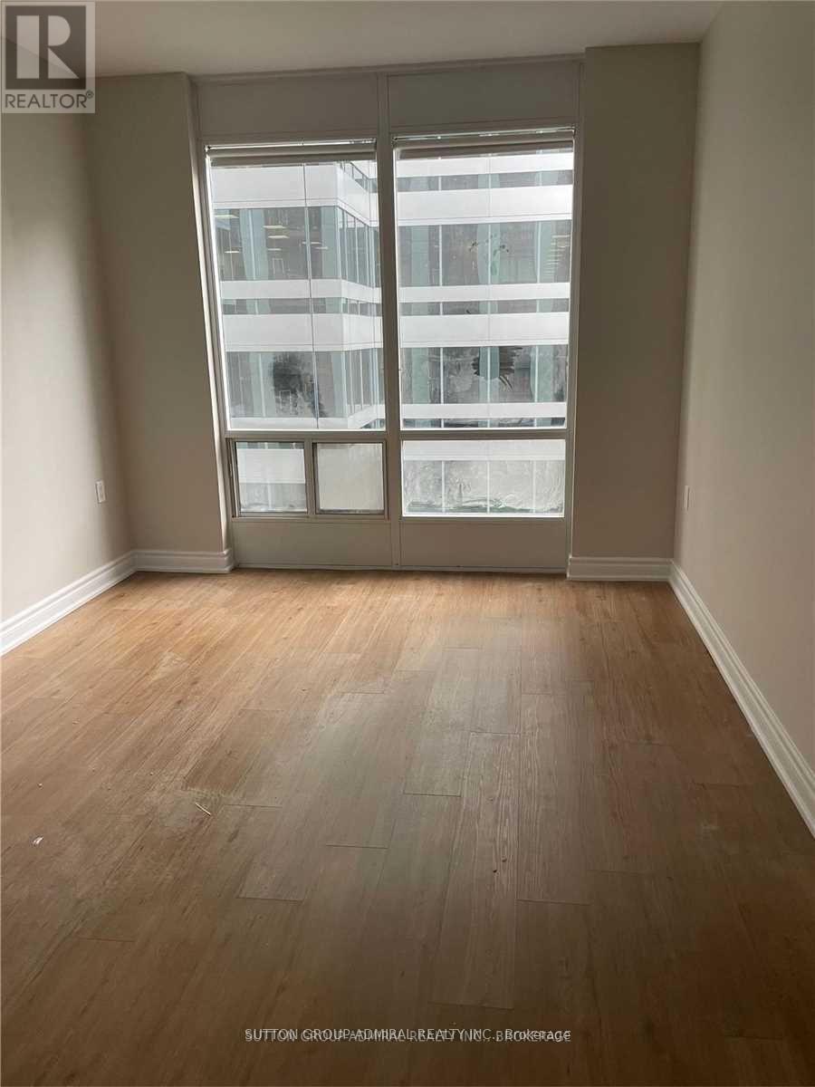 A room with wooden flooring and a large window overlooking a building.