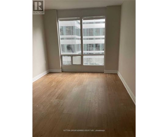 A room with wooden flooring and a large window overlooking a building.