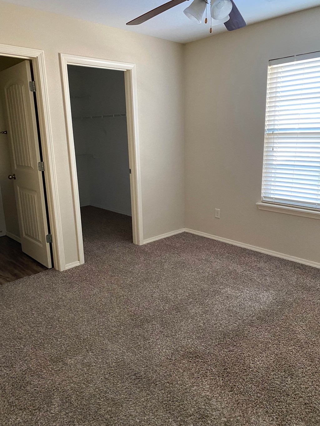 A room with a ceiling fan and a window with blinds.