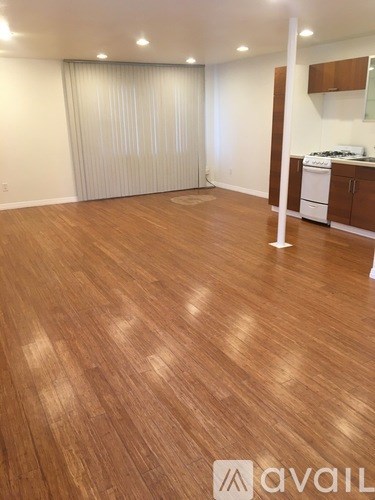 A room with wooden flooring and a kitchen area in the background.