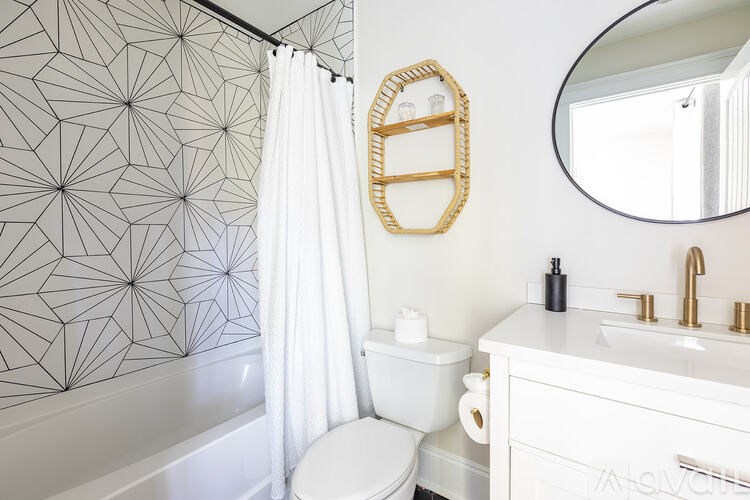 A bathroom with a white toilet, a white sink, a white bathtub, a white shower curtain, a gold mirror frame, and a gold towel ring.
